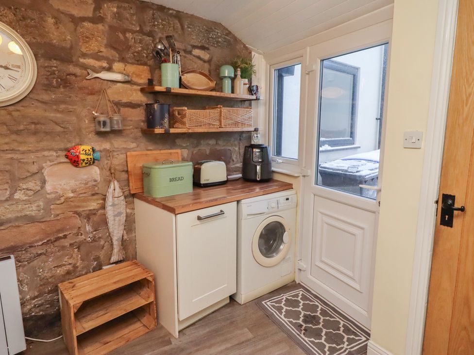 A kitchen with a washing machine and shelf storage at Corner Cottage in Seahouses