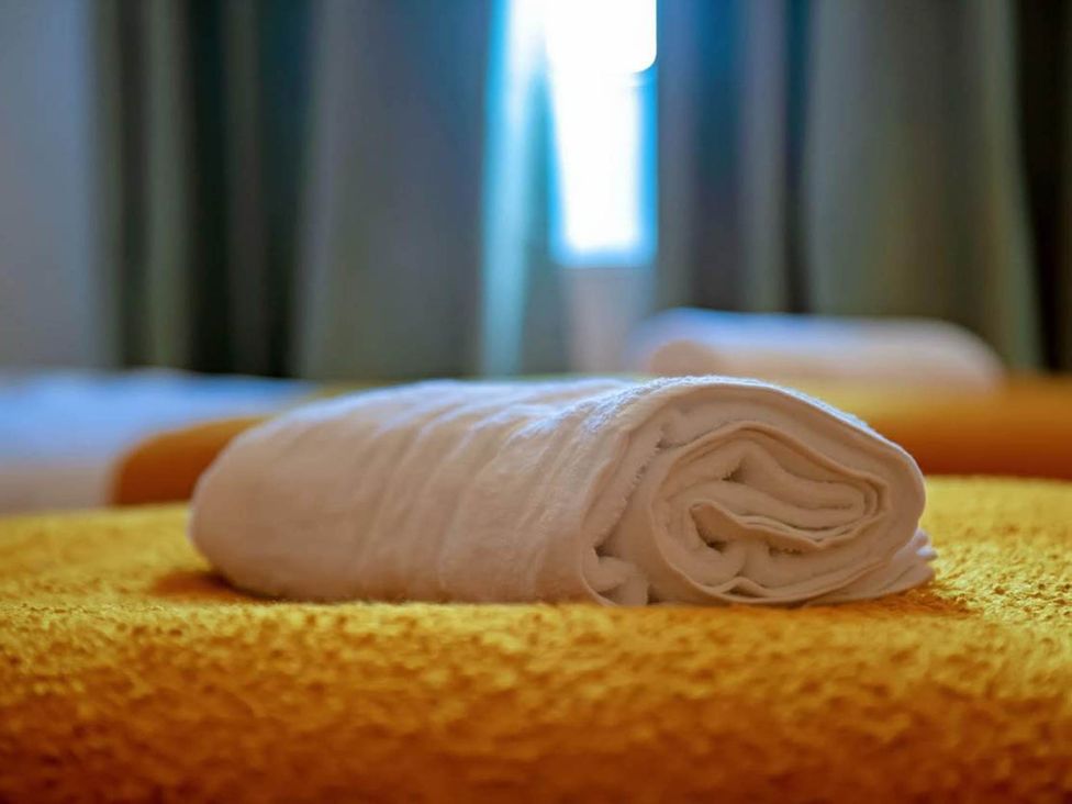 A rolled towel on an orange bedspread in a bedroom