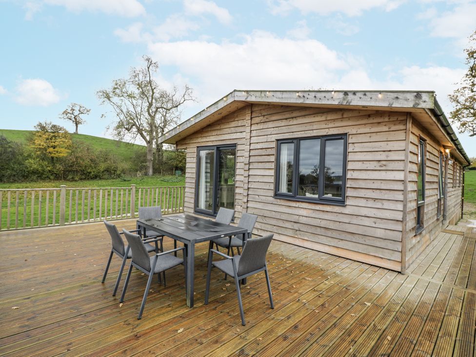 A wooden cabin with a table and chairs on a deck at Willow Lodge in Admaston near Abbots Bromley