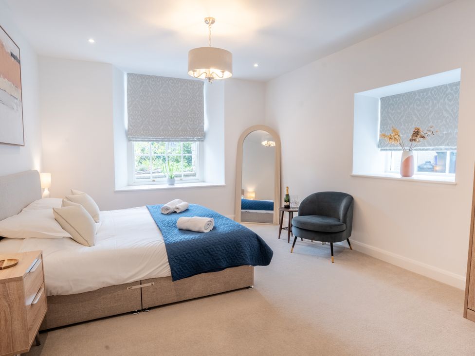 A bedroom with bed, armchair, and mirror at Derwent in Ulverston