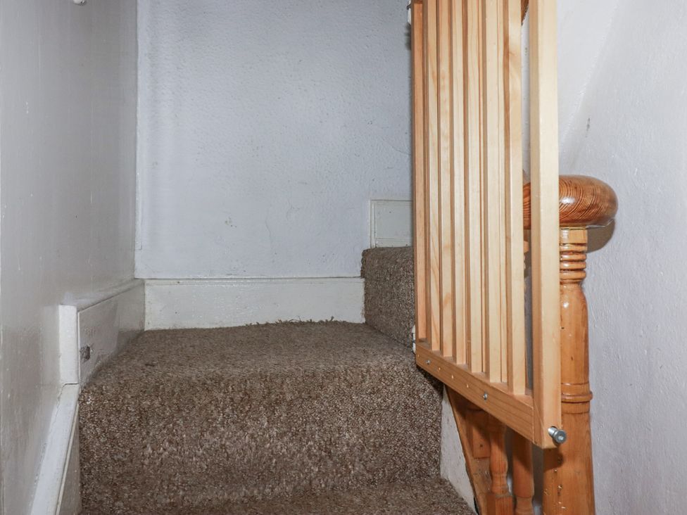 A staircase with a wooden railing and carpet at Blowing House Cottage in Perranporth