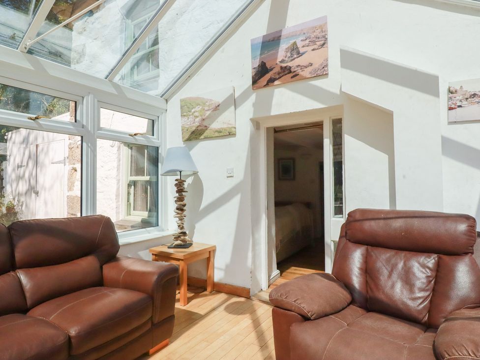 A conservatory with two brown sofas and a lamp at Blowing House Cottage near Perranporth