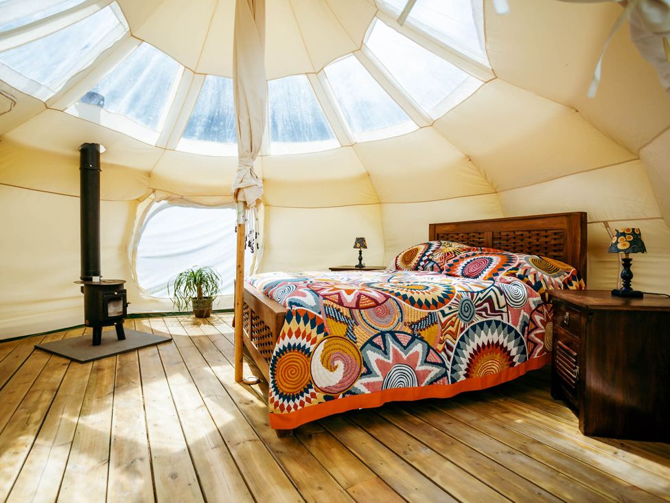 A bedroom with a bed, wood stove, and windows at a glamping site