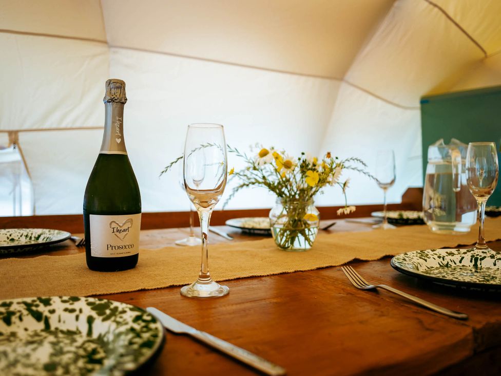 A dining area with a bottle of prosecco and wine glasses at a glamping site