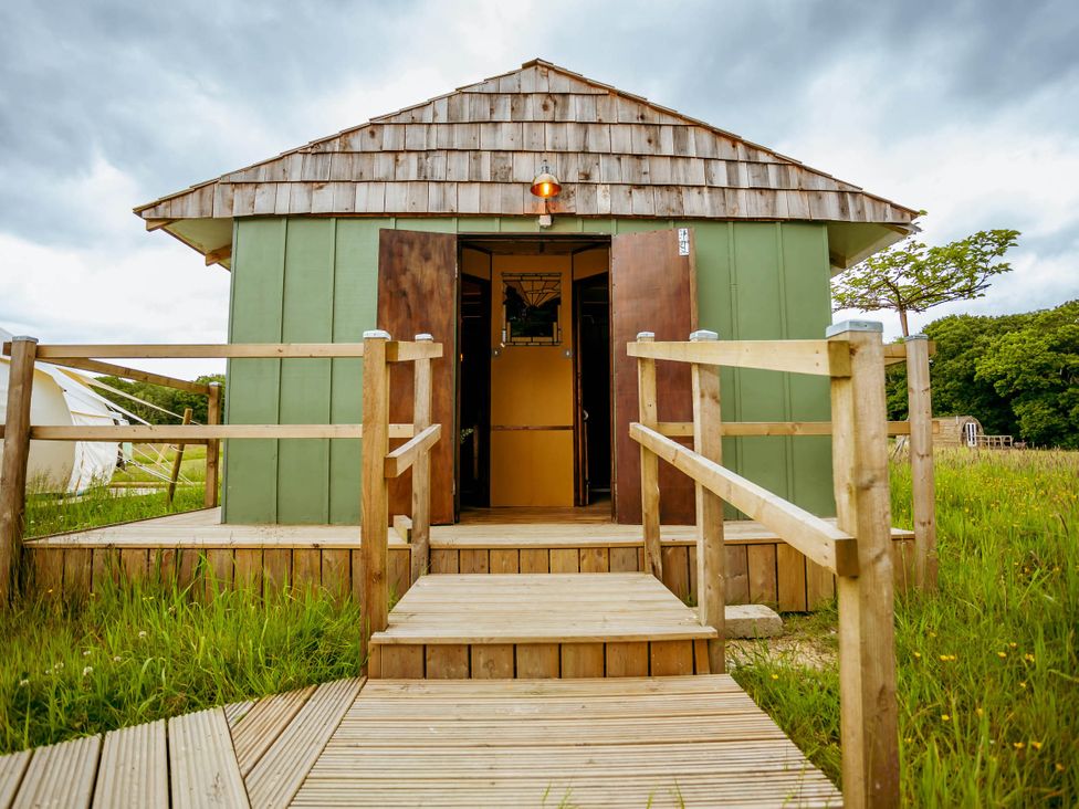 A cabin entrance with wooden steps and railing in a grassy area