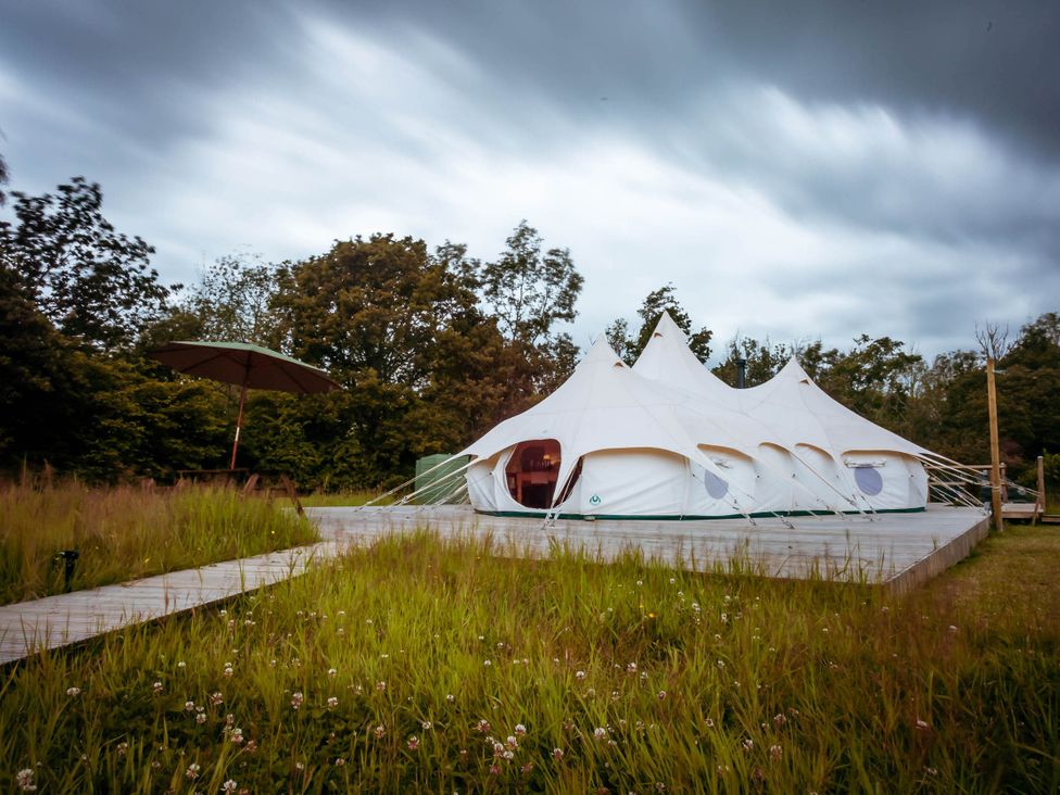 A tent with an umbrella in an outdoor area surrounded by grass and trees at a camping site
