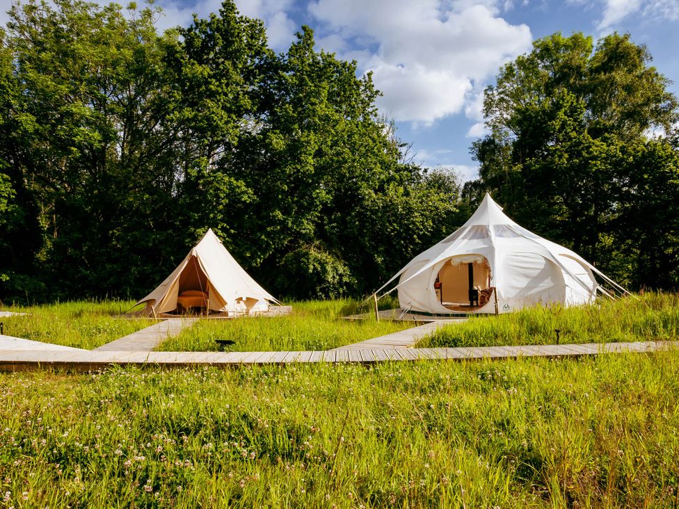 Two tents and a wooden walkway in a grassy area at an outdoor campsite