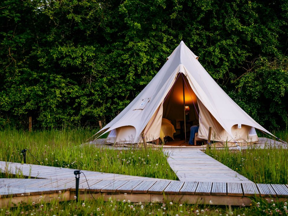 A glamping tent with a wooden walkway in a grassy area at the campsite