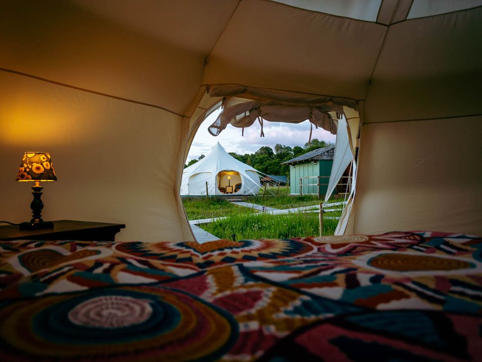 A tent interior with a lamp and a view of an outdoor tent at a camping site