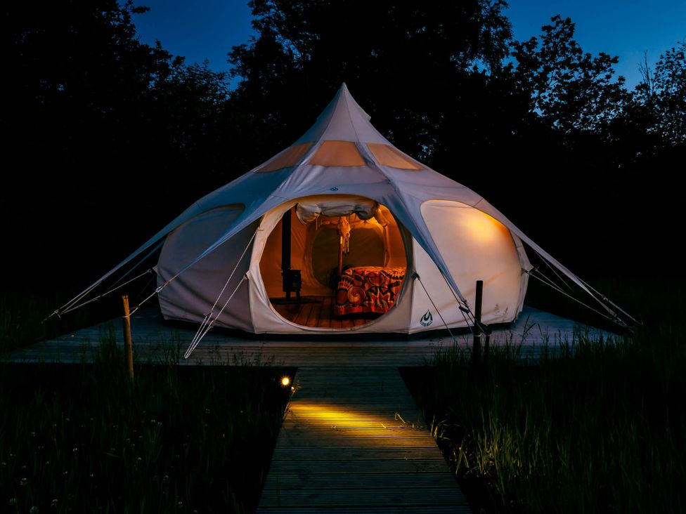 A tent illuminated at night on a wooden platform