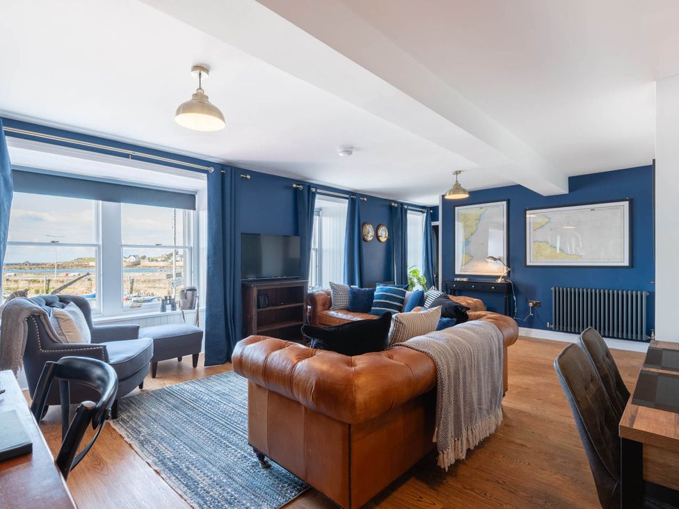 A living room with a sofa and chairs facing a television at a property