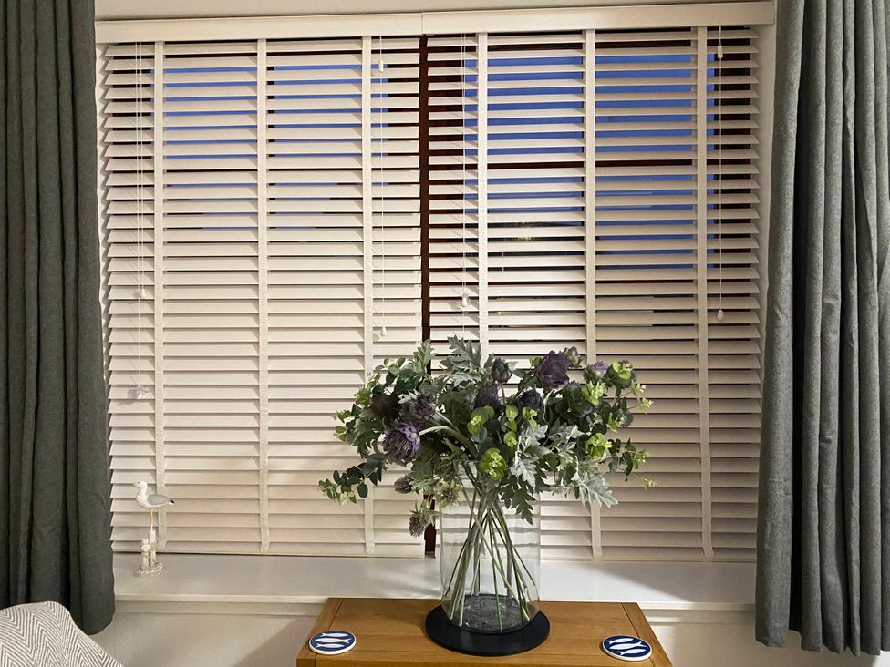 A window with blinds and curtains along with a plant in a vase on a table