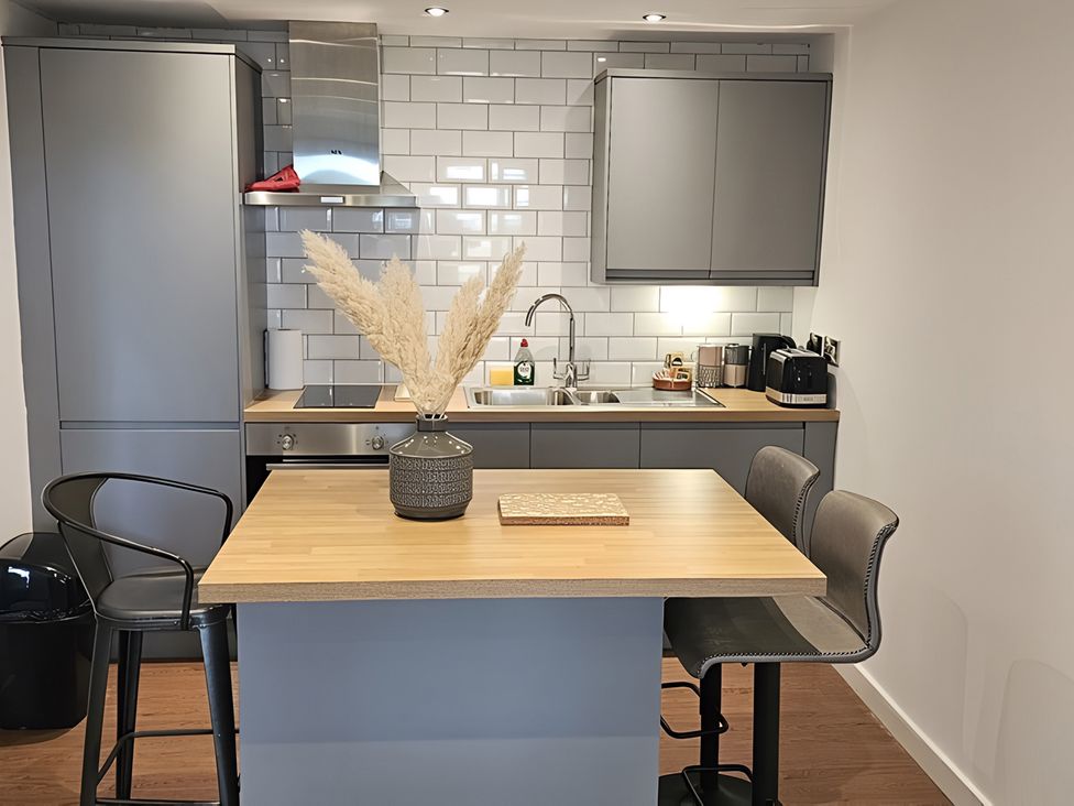 A kitchen with a sink, stovetop, and bar stools at Rutland Apartment 