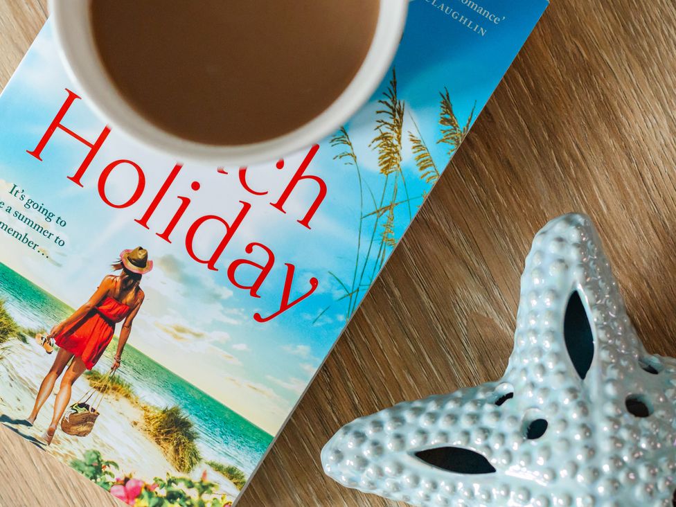 A book titled Beach Holiday with a coffee cup and starfish on a wooden surface at Wee Jules By The Sea