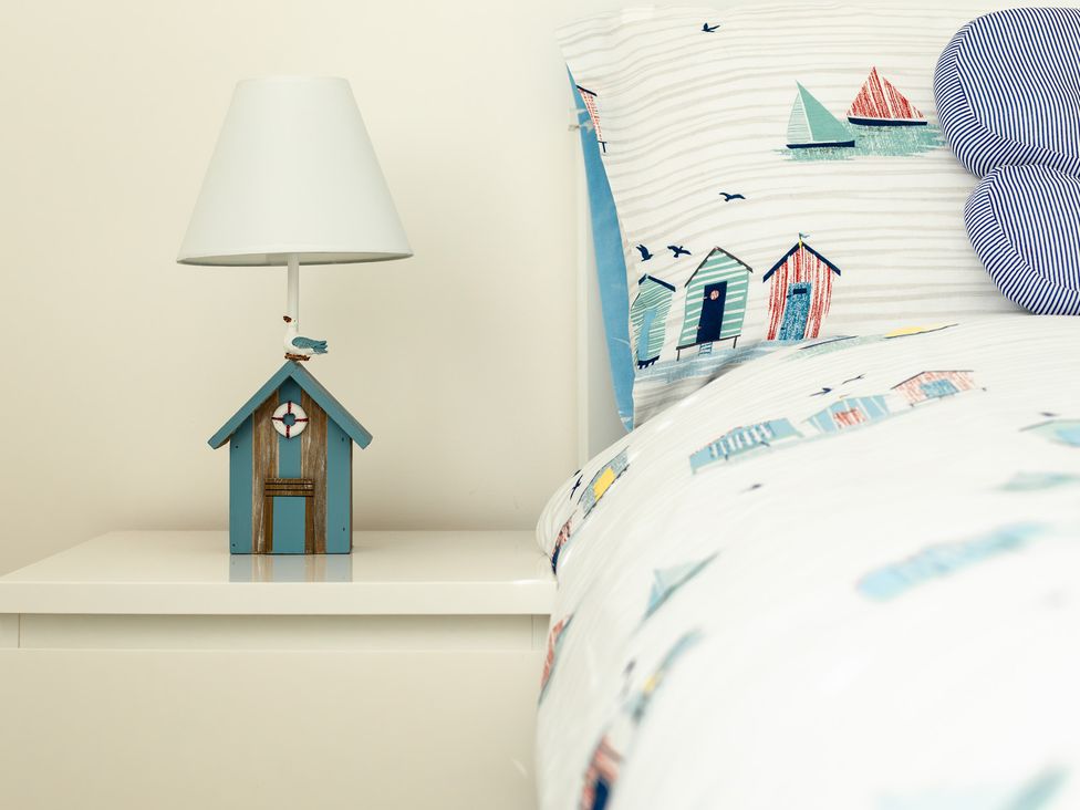 A bedside table with a lamp and bed with patterned linen at Wee Jules By The Sea
