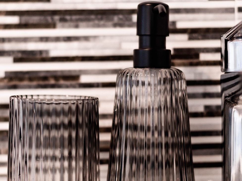 A glass bottle and a drinking glass on a counter with tiled wall at 