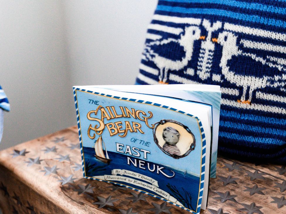A book titled The Sailing Bear of the East Neuk on a wooden table with a decorative pillow
