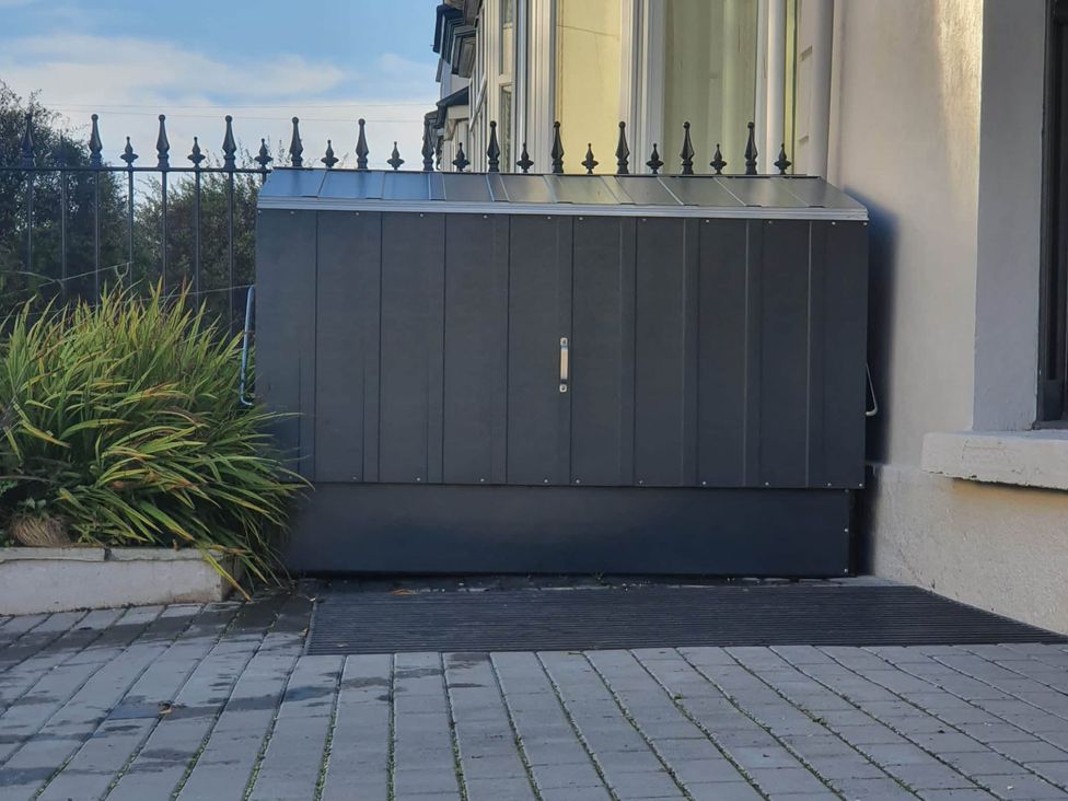 An outdoor storage unit next to a planter with plants beside a fence