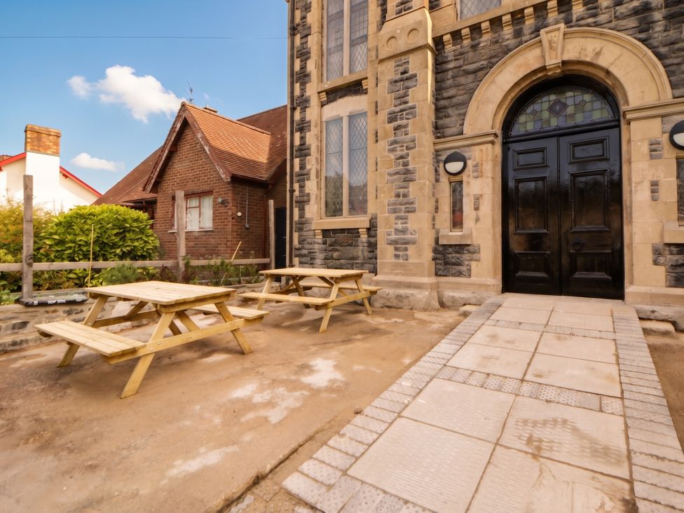 A building entrance with picnic tables and a stone wall at Capel Llani Llanidloes