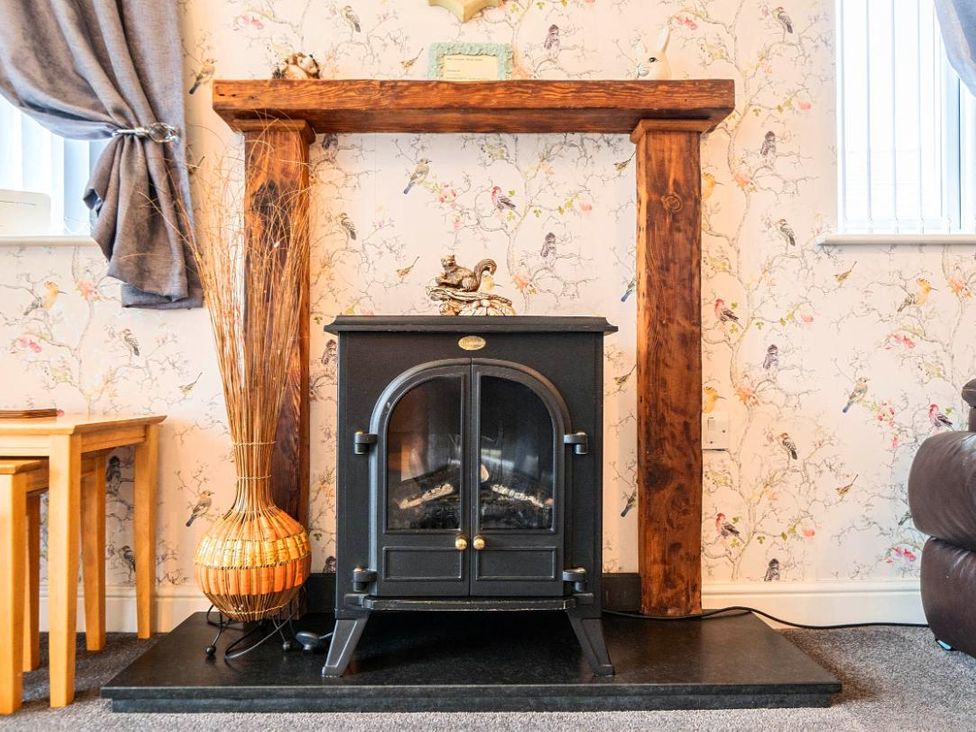A fireplace with a stove and wooden mantel in a living room at Ivy Corner in Bridlington