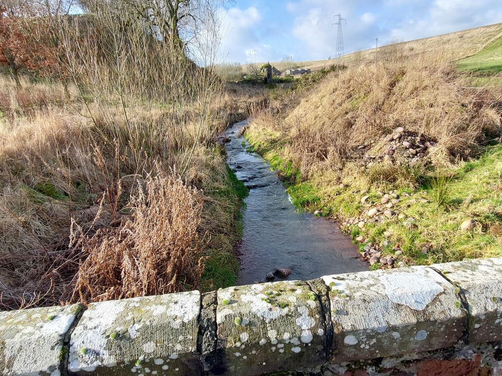 A stream running through grass with a stone bridge nearby at an outdoor location