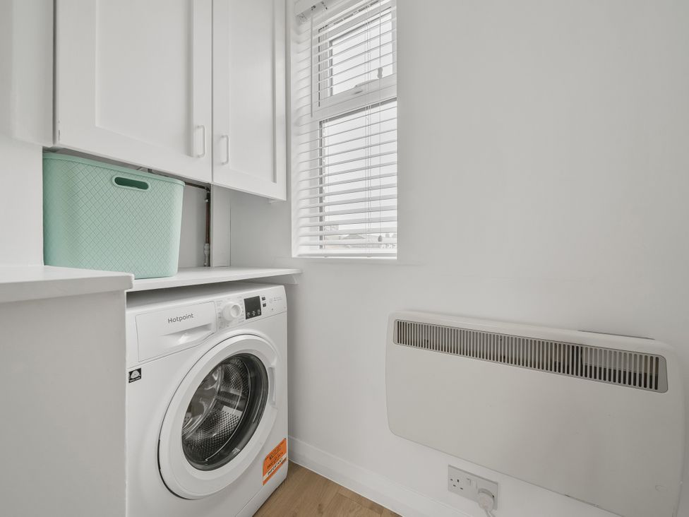 A laundry room with a washing machine and storage cabinet at Red Rose Apartment in Weymouth