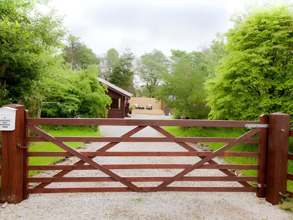 A gate leading to a cabin with trees and gravel driveway at Gisburn Forest Lodge