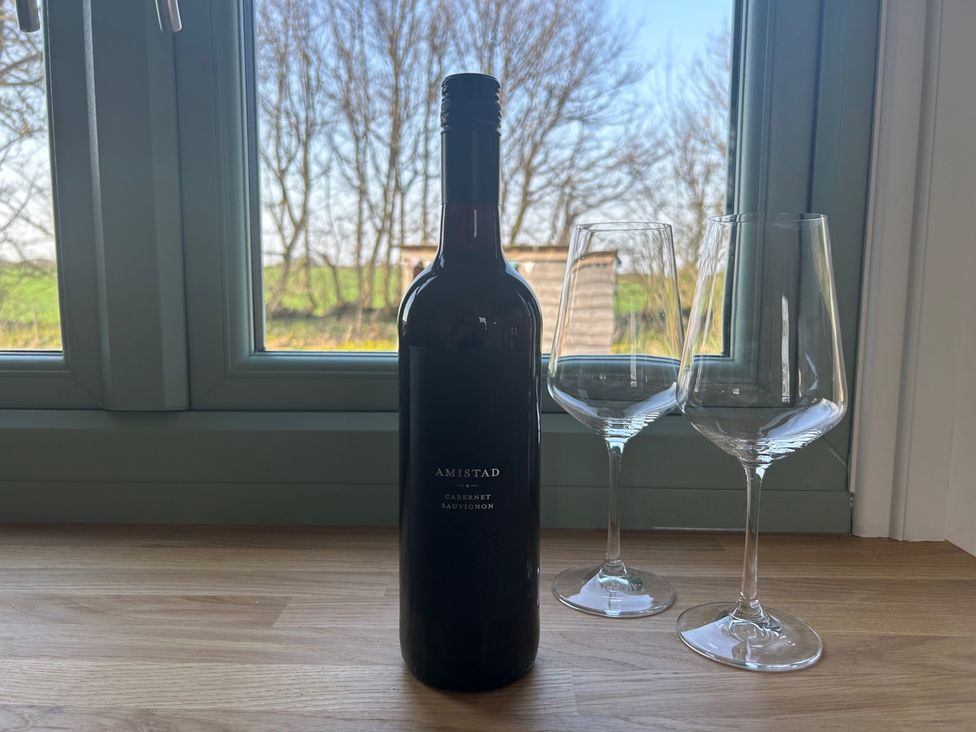 A wine bottle and two glasses by a window at Y Nyth