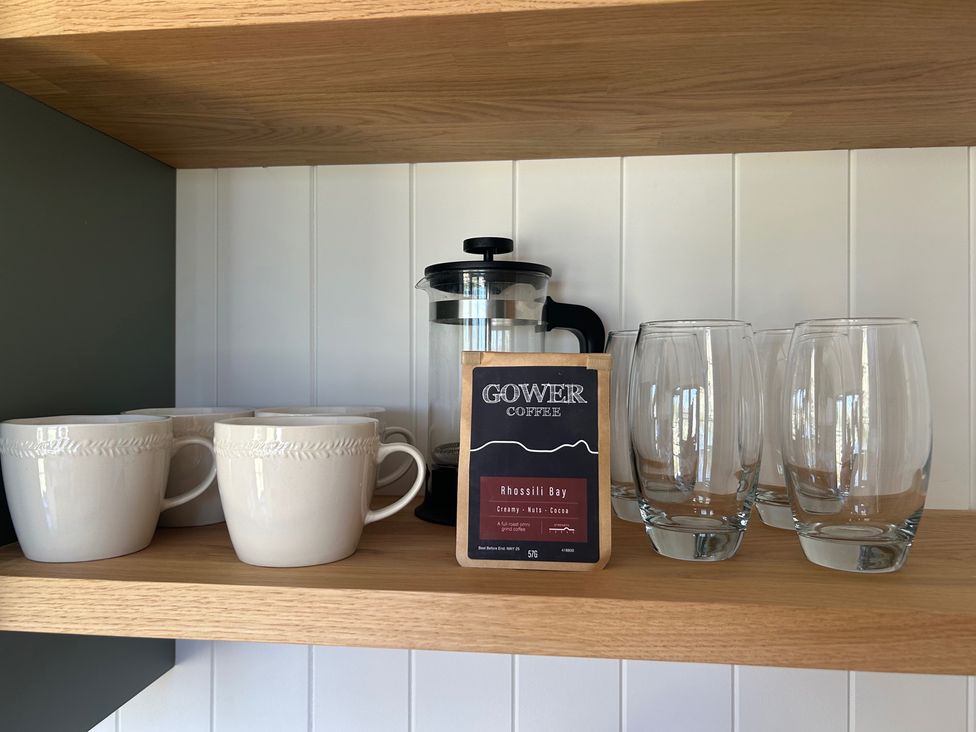 A kitchen shelf with cups, coffee grinder, coffee bag, and drinking glasses at Y Nyth in 