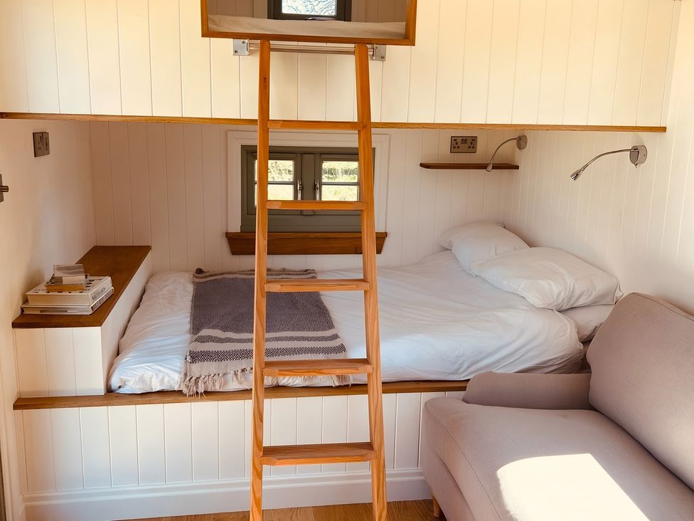 A loft bedroom with a bed and a ladder at Y Nyth