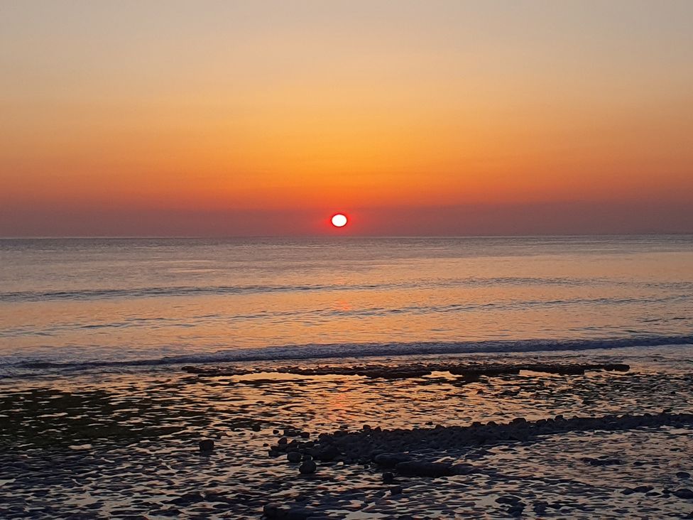A sunset over the ocean with rocks at Y Nyth 