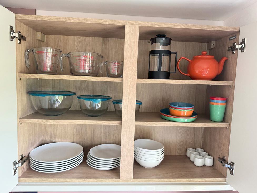 Kitchen cabinet organized with measuring cups bowls plates and teapot at Withi-Gill