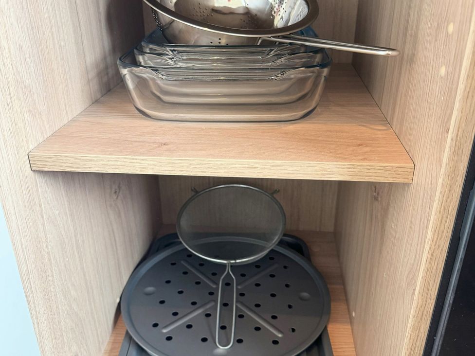 A kitchen storage shelf with glass dishes, a metal colander, and a steamer tray at Withi-Gill