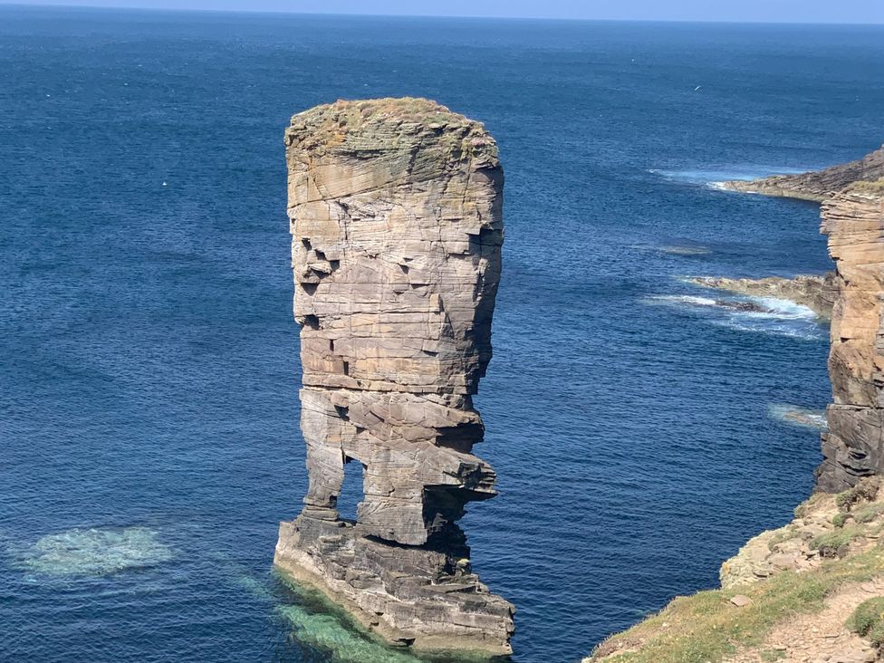 A rock formation standing in water with a clear sky at Withi-Gill