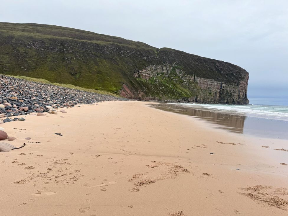 A beach with sand and rocks beside a cliff at Withi-Gill