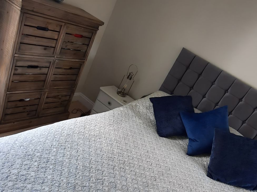 A bedroom with a bed, cushions, bedside table, lamp, and dresser at Lil Nauti