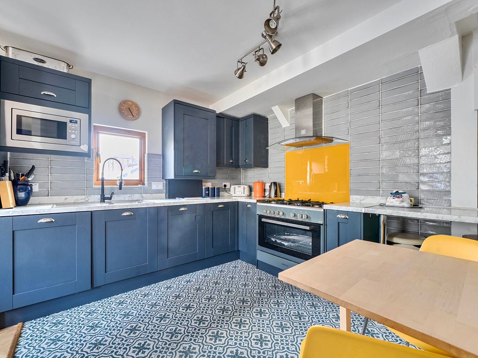 A kitchen with appliances and a dining table at Lil Nauti Fowey