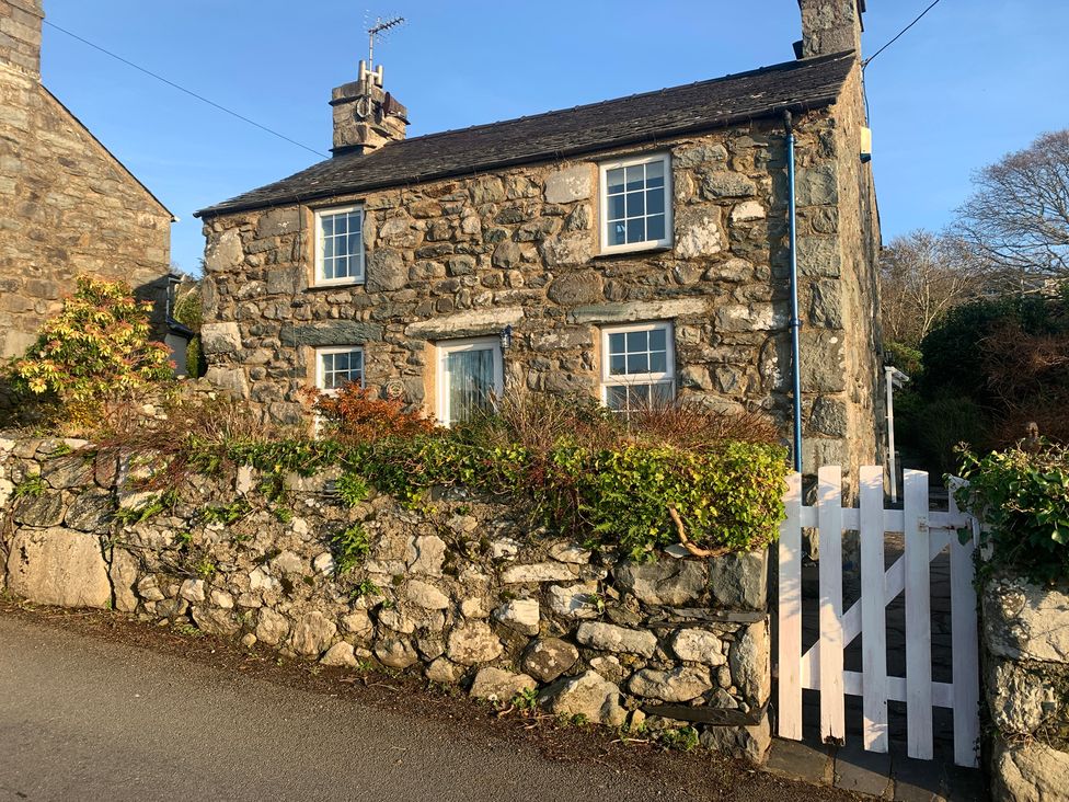 A stone house with a white gate and greenery at Bwthyn Nain