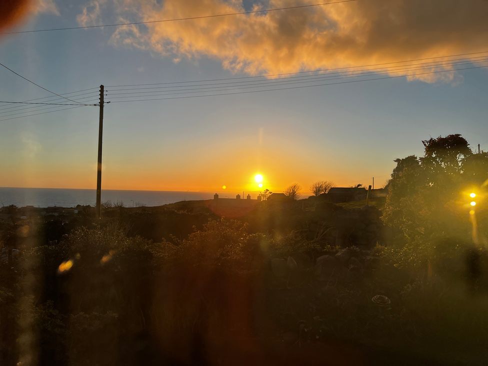 A sunset over the ocean with silhouettes of trees and buildings at Bwthyn Nain