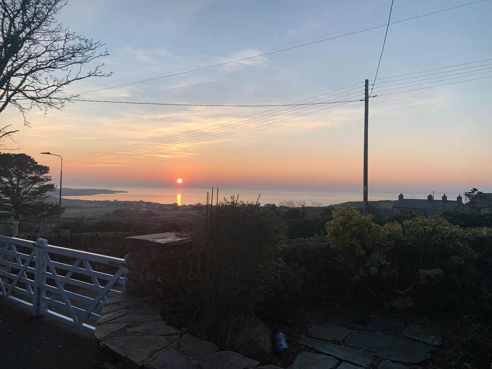 A sunset view over the ocean with trees and a fence at Bwthyn Nain in 