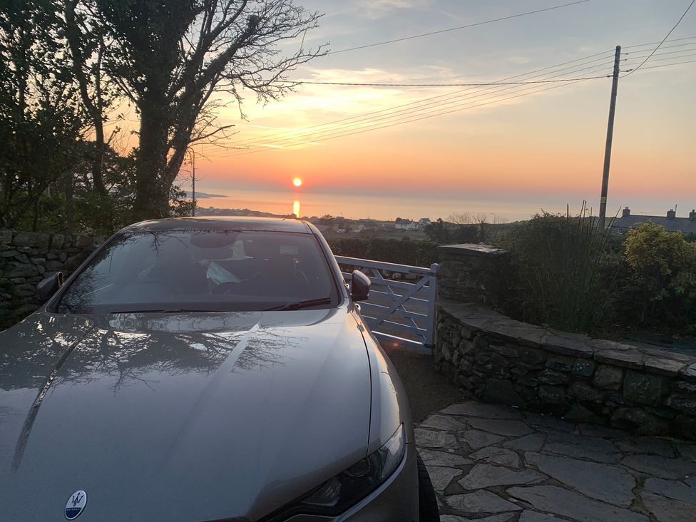 A car parked with a view of the sunset over the ocean at Bwthyn Nain
