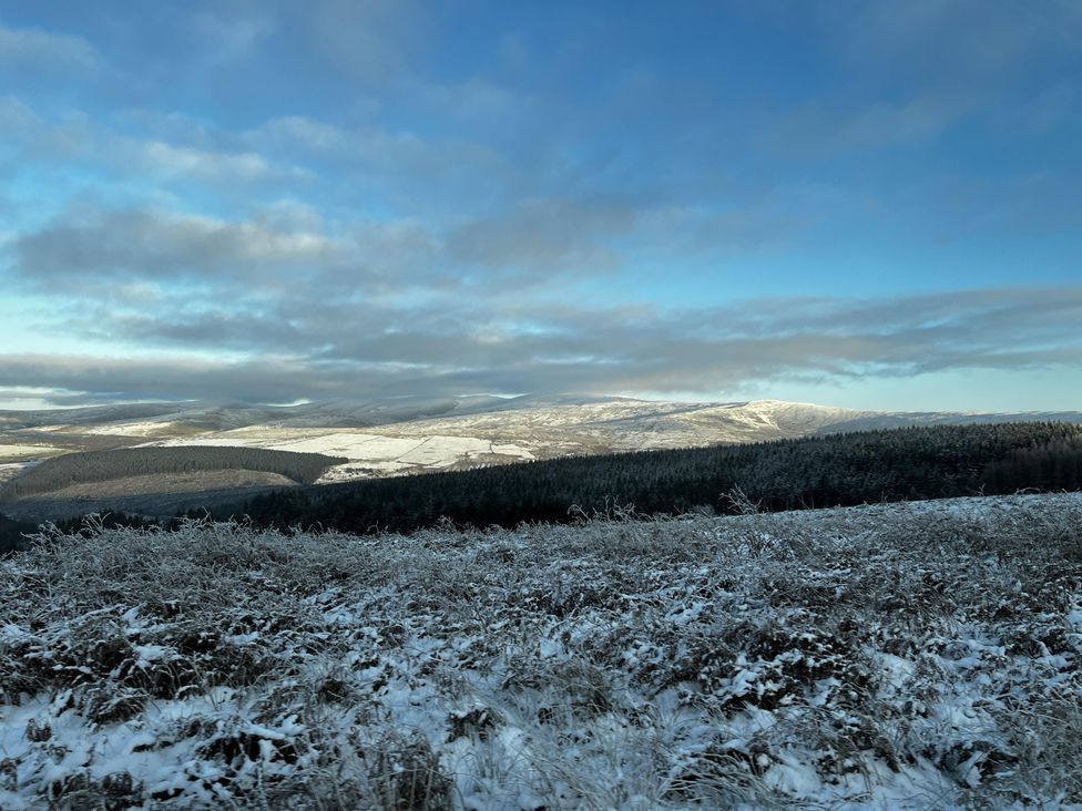 A snowy landscape with mountains and forests at Bwthyn Nain 