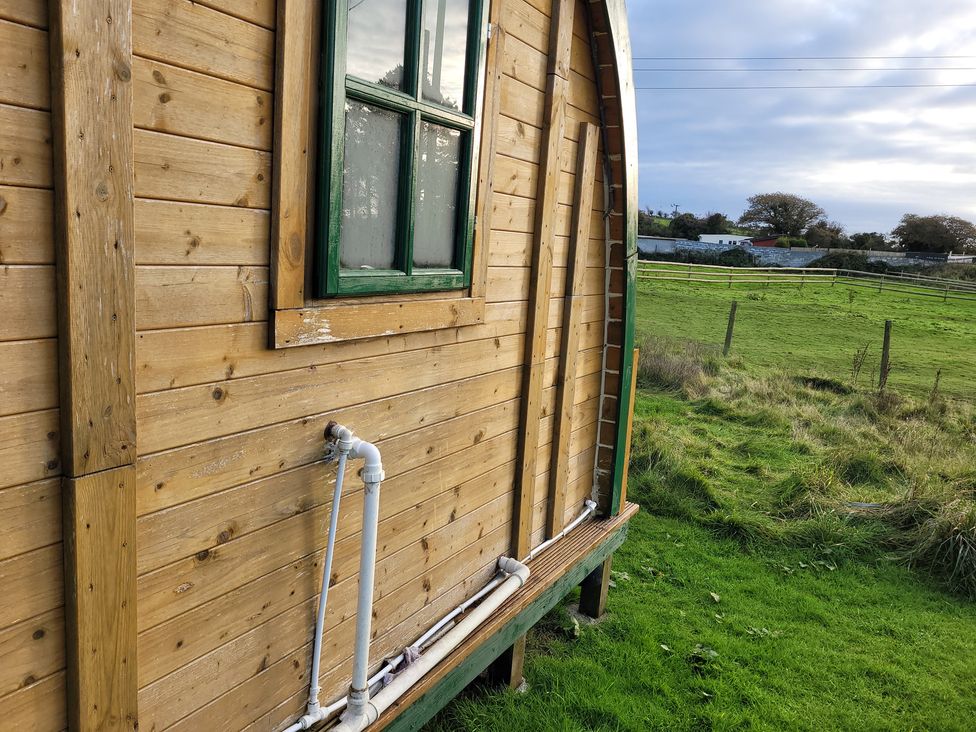 A wooden cabin exterior with a window and water pipe at St Austell Glamping