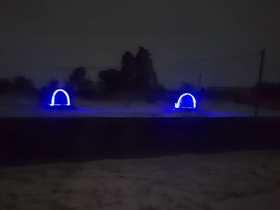 Two blue light structures in a dark outdoor area at St Austell Glamping