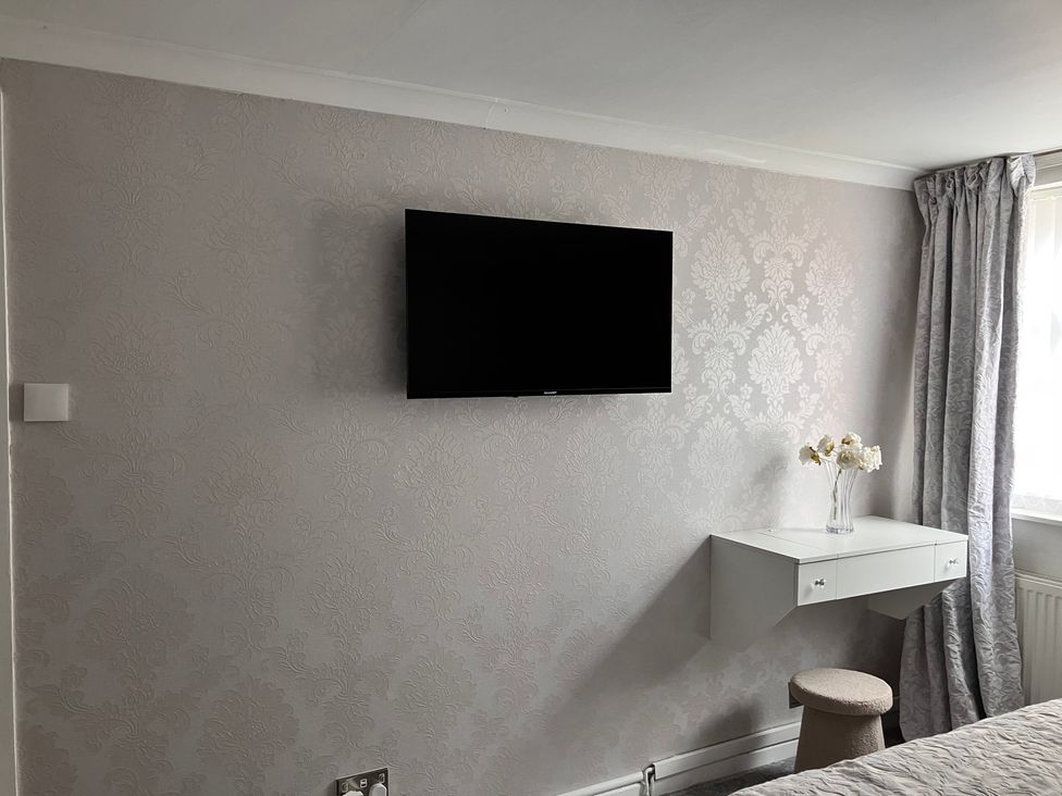 A bedroom with a television, a desk with a vase and flowers, and a stool at Flat 2A