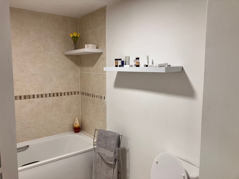 A bathroom with a bathtub and shelf containing cosmetics at Flat 2A