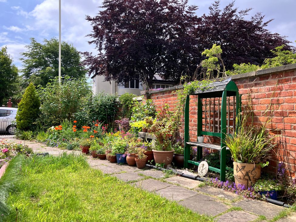 A garden with flower pots and a bench against a brick wall at Flat 2A