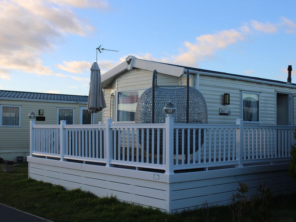 A caravan with a deck and umbrella at a holiday park