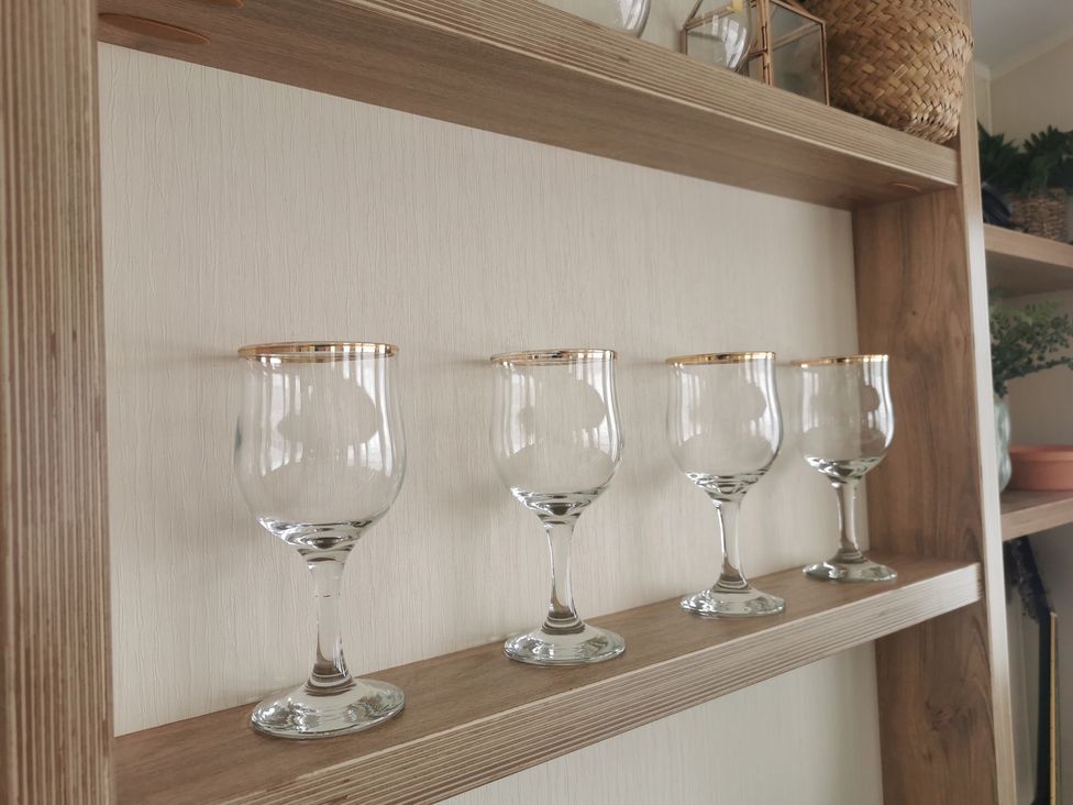 Four glasses arranged on a wooden shelf in a living room