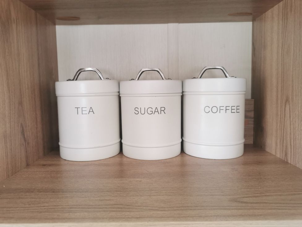 Three canisters labeled tea, sugar, and coffee on a shelf in the kitchen